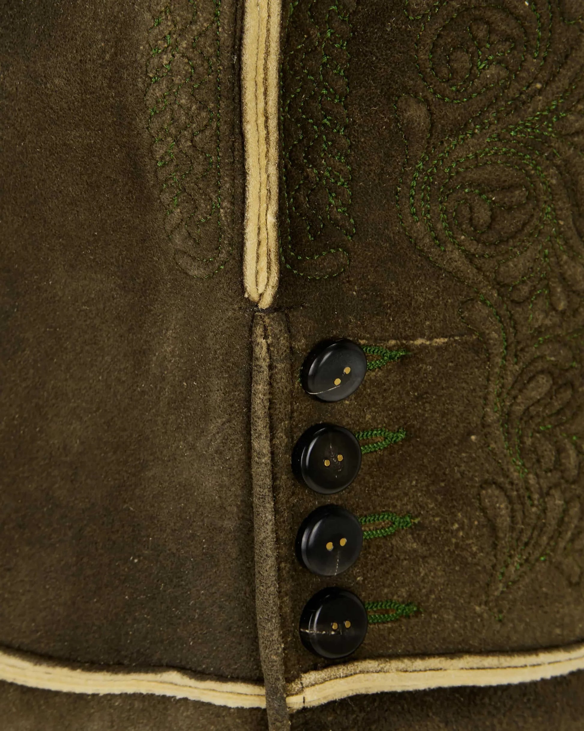 Close-up of a brown jacket with black buttons and intricate green embroidery.